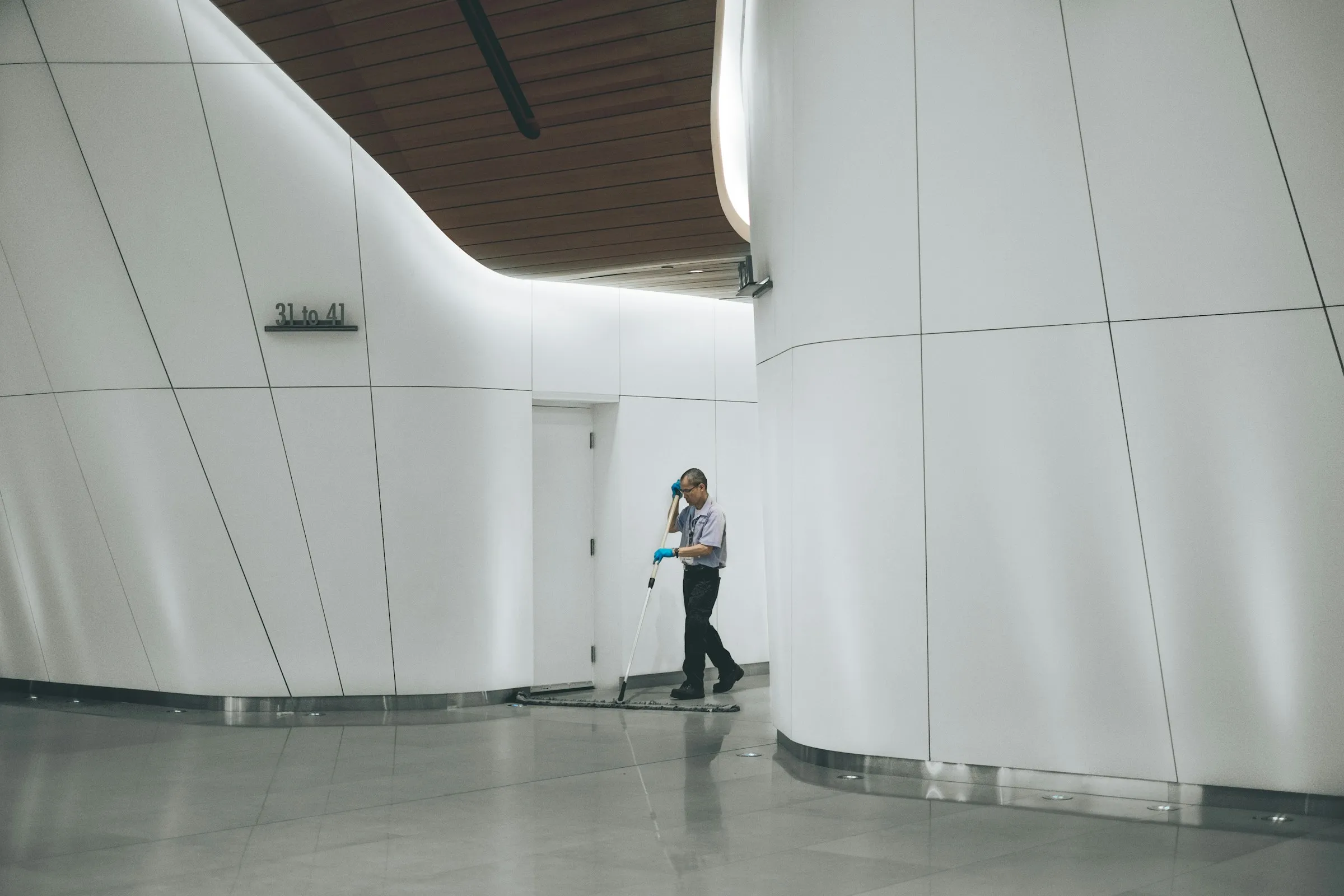 A cleaner mopping the reflective floor of a bright modern corridor.