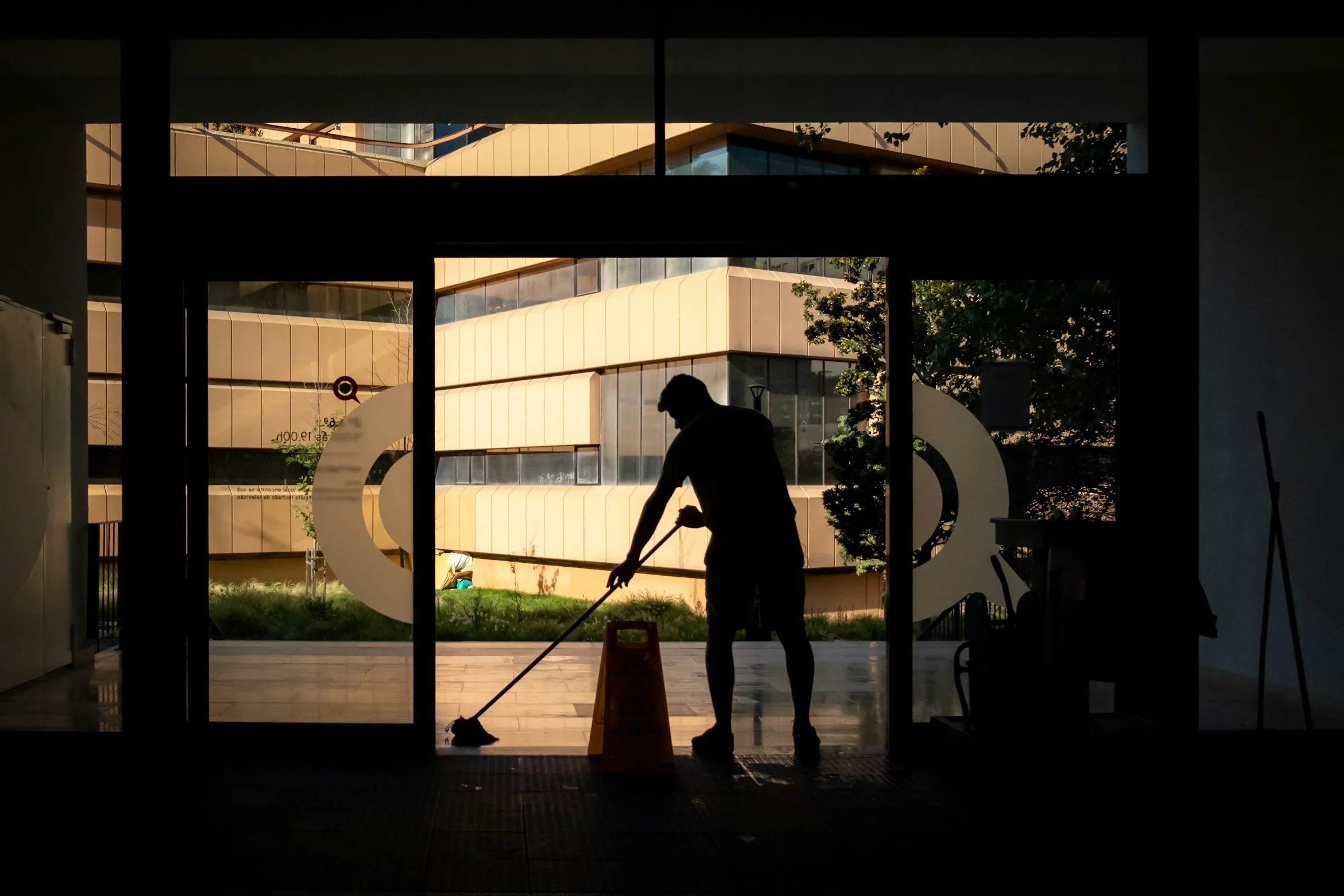 A cleaner mopping a polished commercial entrance in warm evening light.